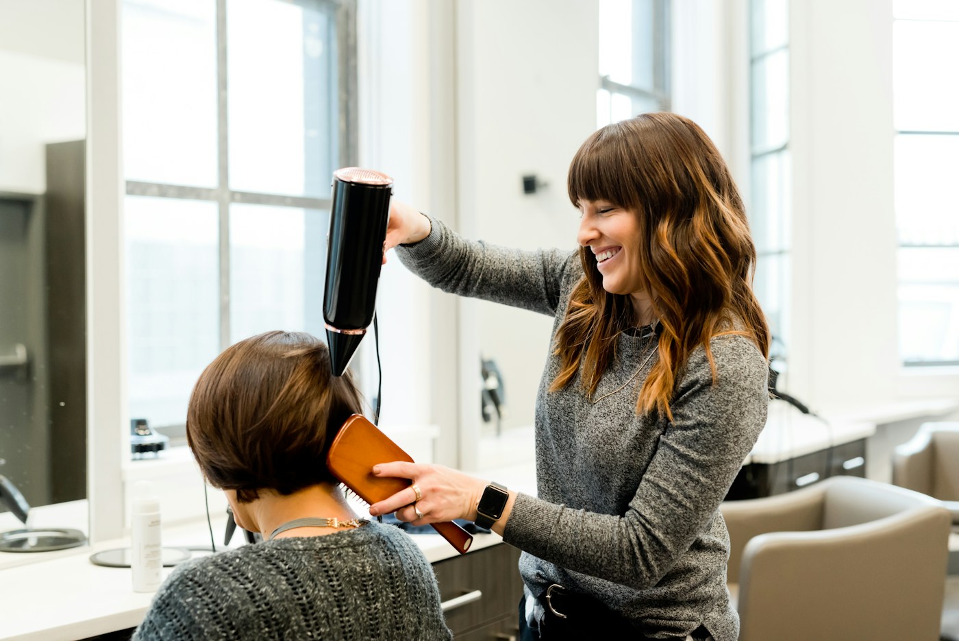 Eine Friseurin föhnt lachend das Haar einer Kundin im Salon
